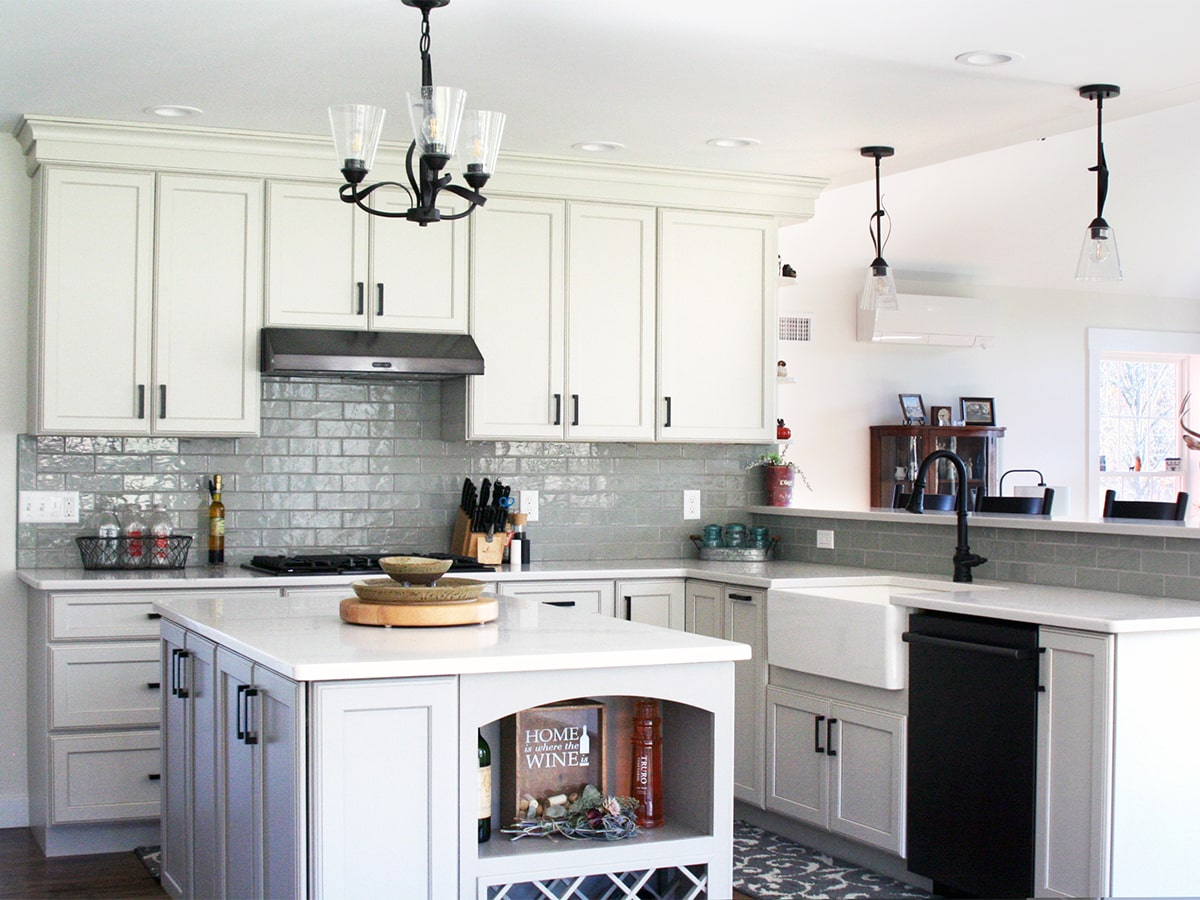 Bright modern kitchen interior with white cabinets, grey tile backsplash, central island with countertop shelving, and contemporary pendant lights