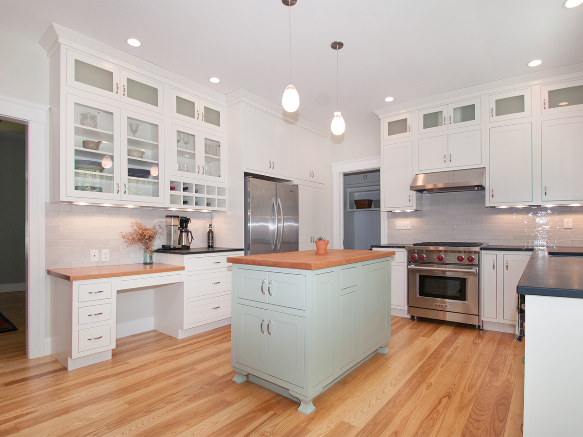 Bright modern kitchen interior with white cabinetry, glass doors, stainless steel refrigerator and range, wooden floor, and a pastel green kitchen island under pendant lights