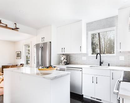 Contemporary open-plan kitchen featuring white shaker cabinets, quartz countertop island with fruit bowl, integrated appliances, pendant lights, and natural light from window