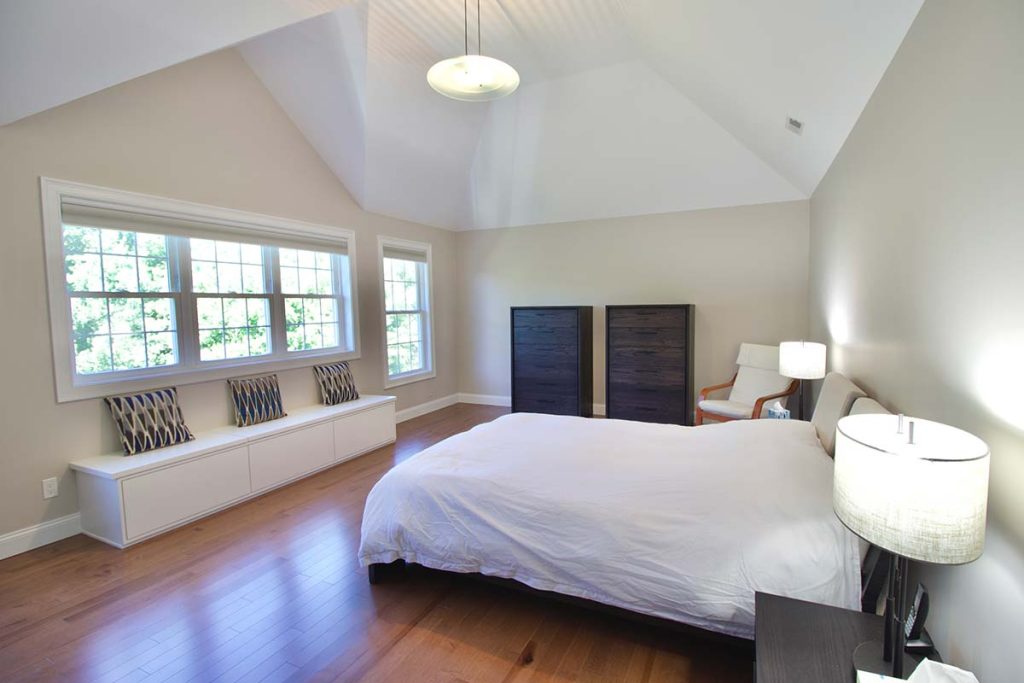 Bedroom renovation and window replacement in Amherst, Massachusetts featuring vaulted ceilings, custom window seating, hardwood flooring, and improved natural light.