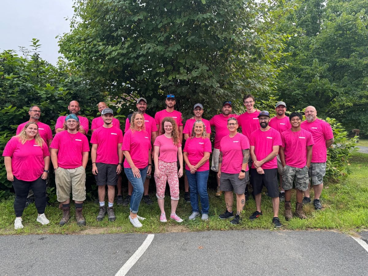 Group picture in front of a tree of 19 members of the Integrity team, all wearing pink t-shirts.